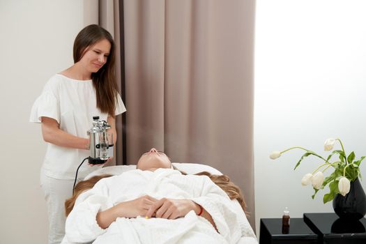 The procedure of steaming the skin of the face of a young woman before cleaning the skin in spa salon