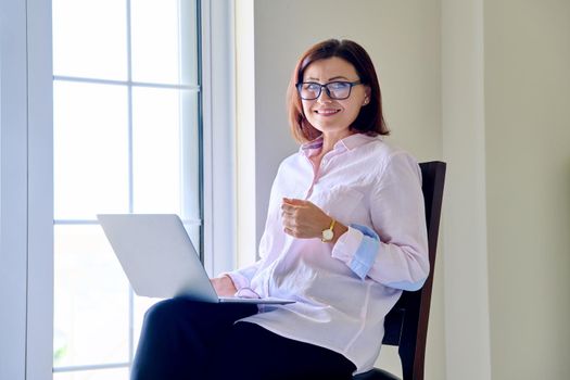 Businesswoman sitting on chair with laptop looking at camera. Female psychologist, psychotherapist, counselor, teacher, mentor, therapist, analyst working online. Technology in business education medicine