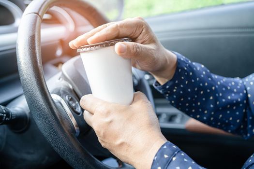 Asian lady holding coffee cup food for drink in car, dangerous and risk an accident.