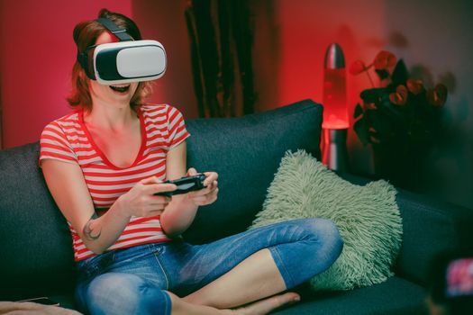 Woman sitting on sofa using vr goggles to play video games. Relaxed woman enjoying video games.