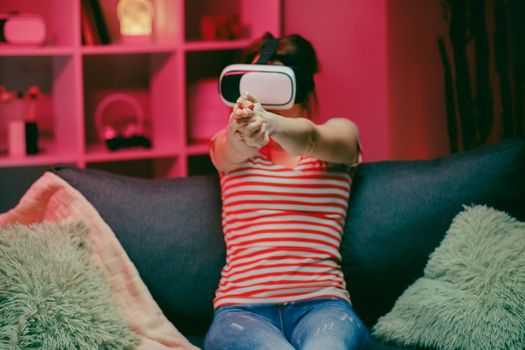 Young woman playing and smiling in the VR headset. Virtual reality helmet on color lighting background