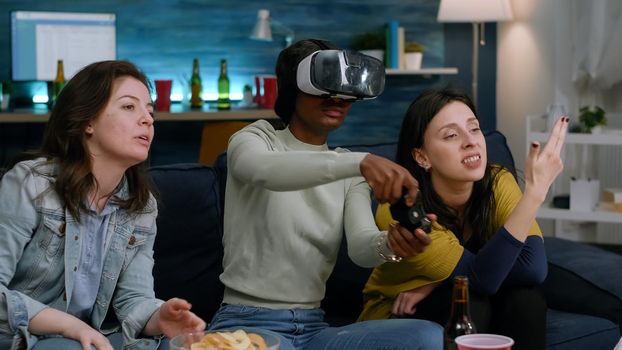 Mixed group of friends guiding afro american woman with virtual reality headset playing simulation game using controller. Afro caucasian female losing online videogame competition