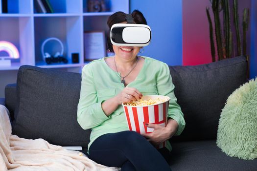 Senior Woman wear VR headset and touch virtual screen at night. Happy Mature Woman Wear Virtual Reality Headset at Home