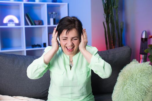 Happy Mature Woman on Headphones Dancing in Home. Aged Female Having Fun Listening Music Using Headset in Modern Interior. Technology, People and Lifestyle Concept