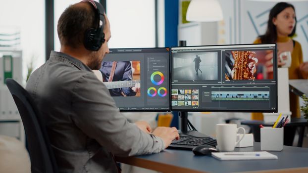 Videographer putting on headset editing video project using post production software working in in digital multimedia company with two monitors. Retoucher processing audio film montage on computer