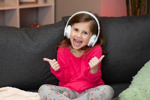 Beautiful Cute Happy Little Girl Listens To Music On Wireless Headphones. Funny Little Girl Dancing, Singing And Moving To Rhythm. Kid Wearing Headphones.
