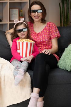 Woman with a little girl Wearing 3d Glasses watching tv and eating popcorn. Family time relax with young girl kid on sofa in living room concept
