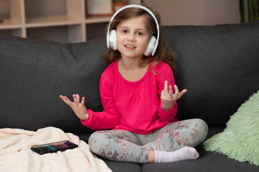 Funny little girl in wireless headphones dancing singing and moving to the rythm. Little girl wearing headphones. Kid in headphones. Happy little girl listening to music with headphones.