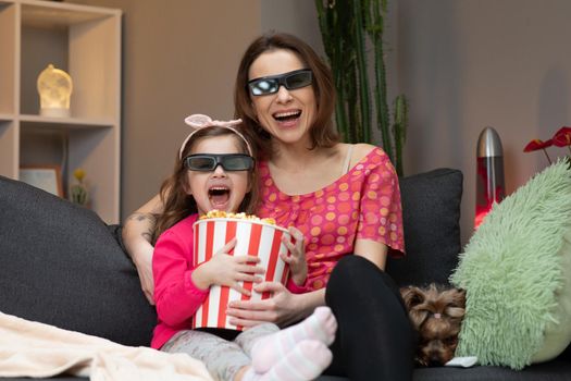 Woman with a little girl Wearing 3d Glasses watching tv and eating popcorn. Family time relax with young girl kid on sofa in living room concept