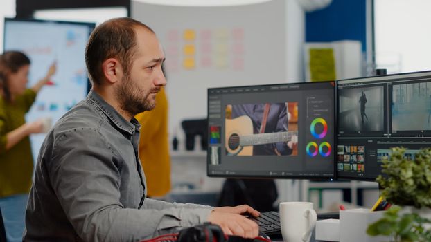 Videographer looking at camera smiling working in creative startup workplace using editing post production software on professional pc with two monitors, processing editing video film footage.