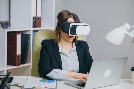 Modern business woman wearing virtual reality glasses in office. Young girl using VR goggles in office. Pretty woman working in augmented reality at workplace.