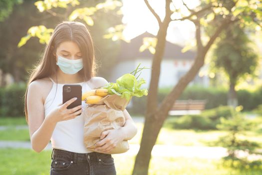 Social distancing. Food delivery. Woman wearing face masks in prevention of coronavirus during quarantine. Woman Using the Mobile Phone. Pandemic.