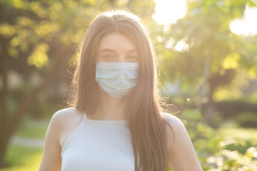 Close up portrait Young woman in medical mask. Female breathes deeply looking at camera. Isolated on park background. Health care and medical concept.