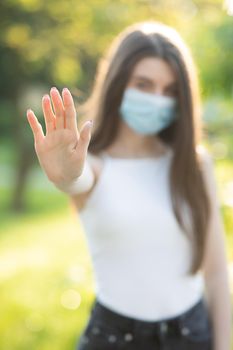 Portrait of a young woman wearing protective mask makes stop sign with hand, saying no, expressing restriction. Concept health and safety, N1H1 coronavirus quarantine, virus protection.