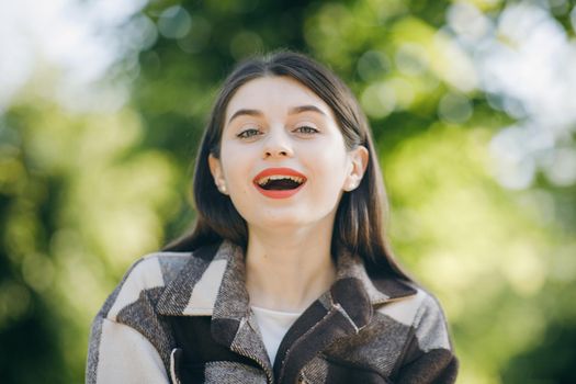 Closeup portrait of pretty girl with long curly hair on street on black trees background. Red lips and smiling to camera.