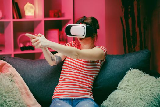 Young woman playing and smiling in the VR headset. Virtual reality helmet on color lighting background