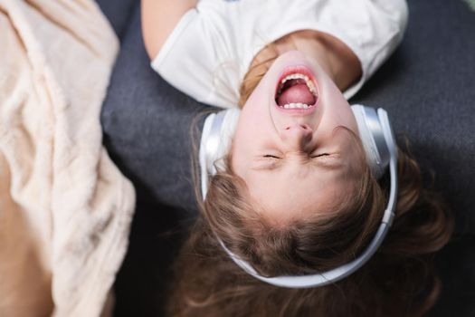 Little girl wearing headphones. Kid in headphones. Happy little girl listening to music with headphones. Funny little girl in wireless headphones dancing singing and moving to the rythm.