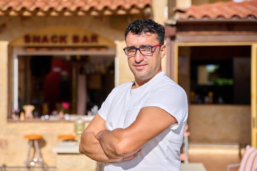 Portrait of positive confident middle aged man wearing glasses with crossed arms. Smiling male cafe bar owner looking at the camera. Small business, 40 people, concept ownership