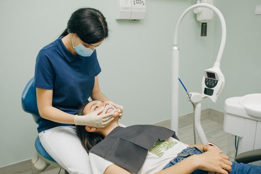 Female dentist in medical white latex gloves puts rubber dam on a patient in a dental clinic. Cleaning teeth. Modern dental office.