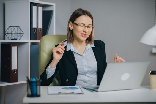 Online internet shopping checkout with credit card payment. Business Woman Shopping Online with Laptop in Office. Young Woman Hold Bank Credit Card in Hand and Buying From Computer