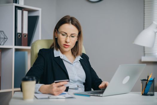 Online internet shopping checkout with credit card payment. Business Woman Shopping Online with Laptop in Office. Young Woman Hold Bank Credit Card in Hand and Buying From Computer.