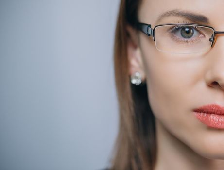 Close up of female eye with glasses isolated on background with copy space. Beautiful half face woman in glasess llooks into the camera.