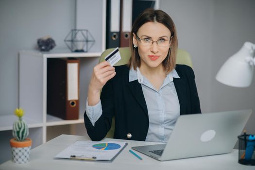 Business Woman Shopping Online with Laptop in Office. Young Woman Hold Bank Credit Card in Hand and Buying From Computer.