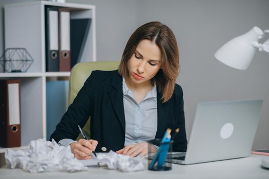 Businesswoman typing his piece of art, crumpling and wasting a sheet of paper dissatisfied with result. Crumpled pieces of paper.