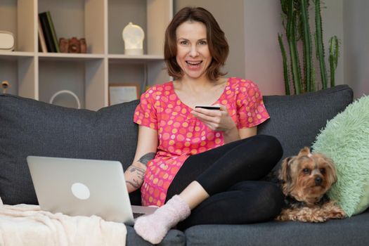 Attractive young Caucasian woman shopping online while entering a credit card number on the laptop computer at home. Inside