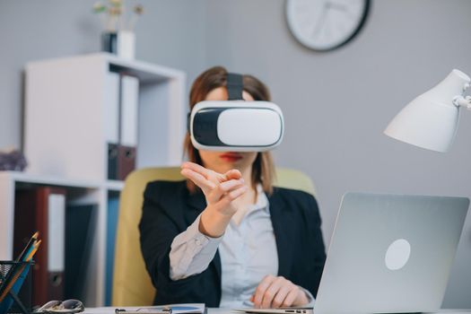 Modern business woman wearing virtual reality glasses in office. Young girl using VR goggles in office. Pretty woman working in augmented reality at workplace.