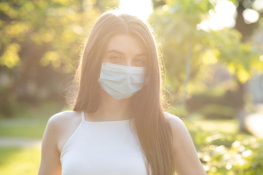 Close up portrait Young woman in medical mask. Female breathes deeply looking at camera. Isolated on park background. Health care and medical concept.