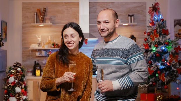 Festive man and woman using video call conference to celebrate christmas eve, clinking glasses of champagne. Couple enjoying holiday festivity from home, using remote communication.