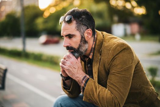 Depressed businessman with beard sitting on the bench in the city.