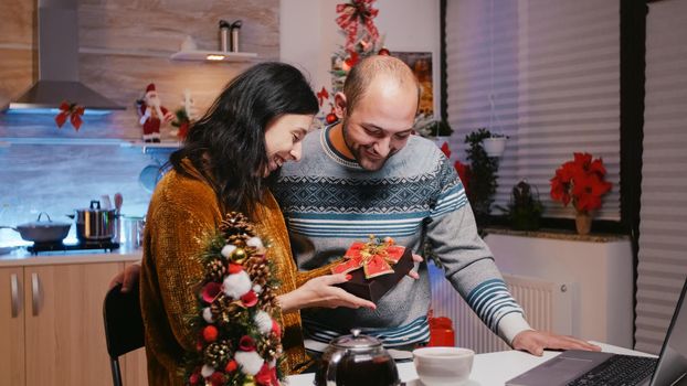 Couple holding present while talking to family on video call communication. Man and woman feeling festive, receiving gift from family on online remote conference for christmas eve.