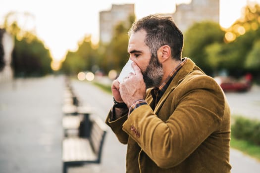 Modern businessman is blowing nose while sitting on the bench in the city.