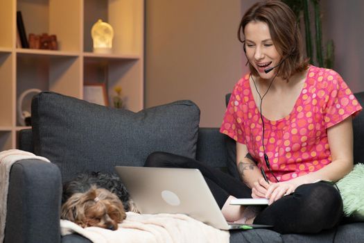 Happy young woman wear headset communicating by conference call speak looking at computer at home. Video chat job interview or distance language course class with online teacher concept