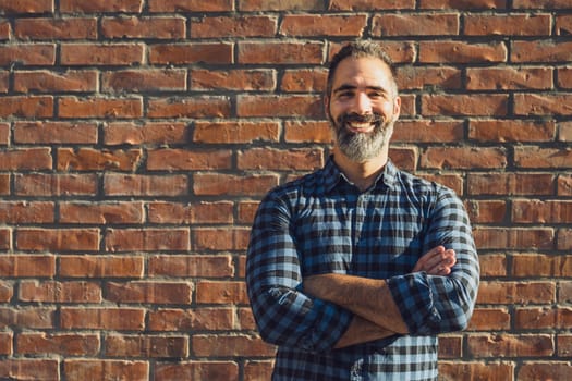 Portrait of modern businessman with beard standing in front of brick wall outdoor.