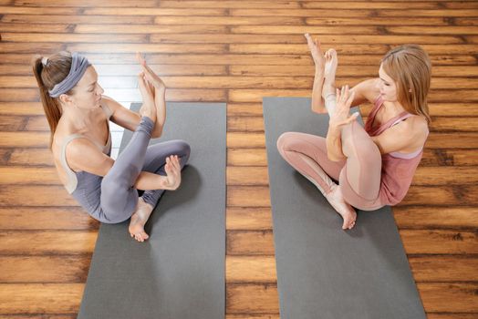 Two sporty women practice yoga in light gym. Fitness, stretching practice, group of two attractive girls doing yoga