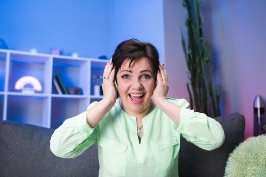 Technology, People and Lifestyle Concept - Happy Senior Woman in Headphones Listening to Music at Home. Positive Meloman Singing to Music. Active Modern Life After Retirement