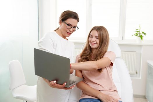 Female doctor working with patient while using laptop in clinic. Beauty doctor consults patient. Cosmetologist and beauty surgeon concept