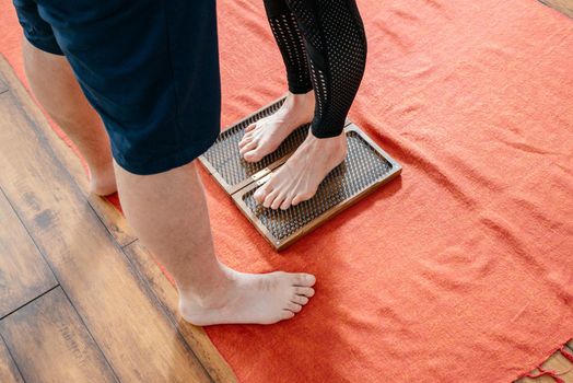 Man helping woman to stand on sadhu yoga board