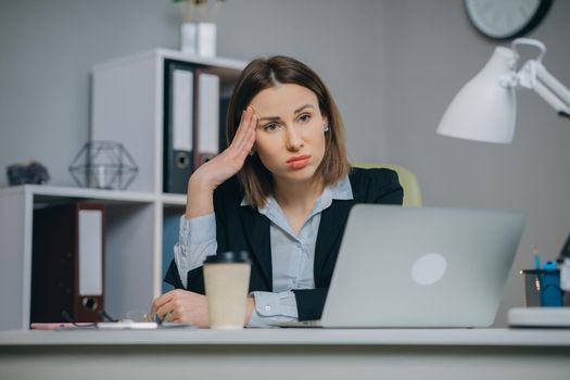 Tired woman in glasses sitting at the laptop computer while working in the office, then almost falling asleep and waking up. Indoor