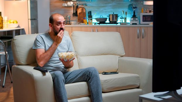 Sport football fan watching game late at night while enjoying popcorn, cheering for favourite football team. Championship entertainment match alone television, soccer fan looking at competition