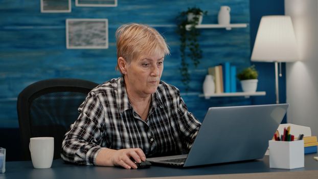 Senior mature older woman watching business training, online webinar on laptop computer remote working, reading, analysing statistics from home. Old retired businesswoman typing, writing project