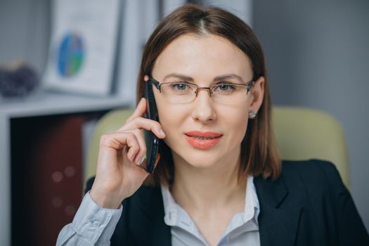 Successful Business Woman in her own Office Talking on the Phone while sitting at the table. Success concept.