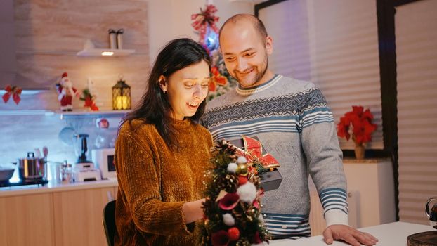 Man giving present box to woman for christmas eve celebration. Festive couple celebrating winter holiday with gifts for seasonal festivity. Cheerful woman receiving gift from partner.