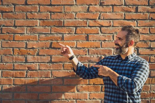 Portrait of modern businessman with beard gesturing while standing in front of brick wall outdoor