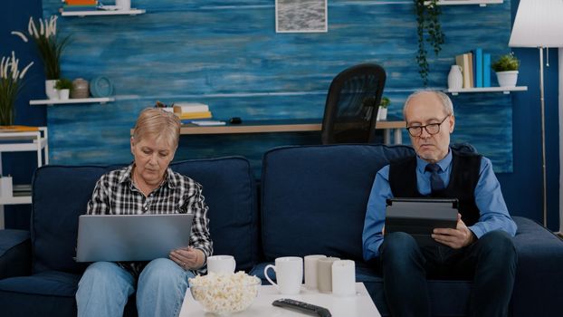 Senior couple in living room using modern gadget and technology to connect with internet. Modern old person browsing informations, surfing the web and connecting with the world