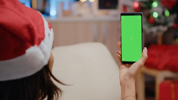 Close up of adult vertically holding smartphone with green screen. Festive woman looking at chroma key screen designed with isolated mockup template and background. Person using technology
