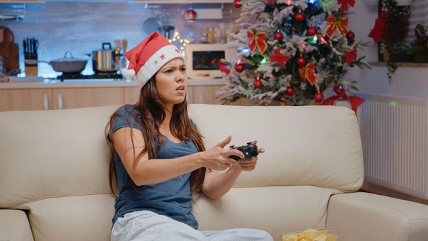 Sad person playing video games with controller on console at television. Festive woman on holiday feeling frustrated about losing play on tv with joystick for christmas eve celebration.